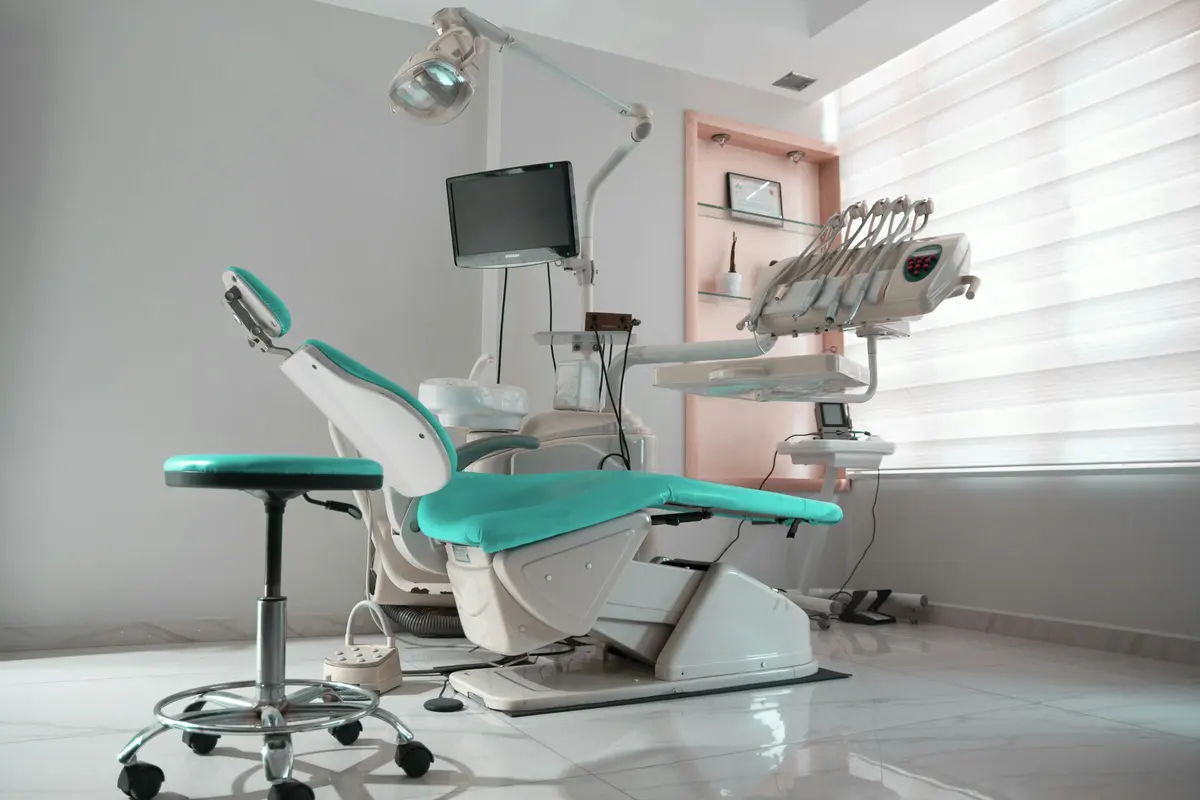A bright dental operatory with a teal treatment chair beside a tall window