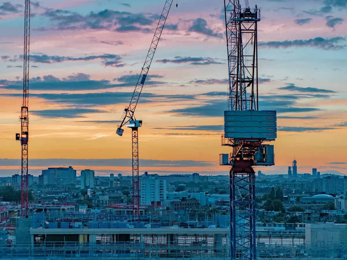 Tower cranes against a blue and amber dusk sky above a city under construction