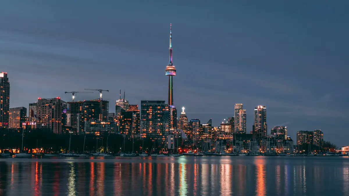 The Toronto skyline and CN Tower at dusk, seen across the lake, with warm lights reflected in the water